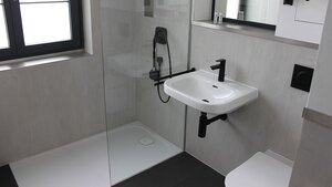 Eine bodenebene Dusche mit Duschboard und Glastrennwand.